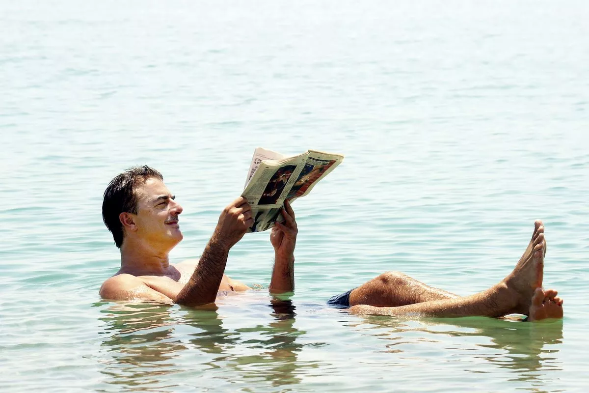 Крис Нот читает газету, плавая в богатых лечебными минералами водах Мертвого моря на юге Израиля