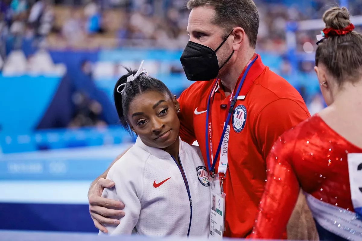 Тренер Лоран Ланди обнимает Симону Байлз после того, как она получила травму и вышла из командного финала на летних Олимпийских играх 2020