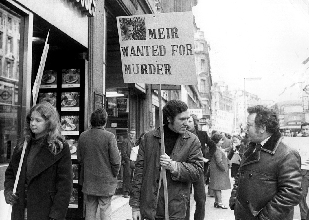 Питер Хейн, лидер молодых либералов, возглавляет демонстрацию, держа плакат «Меир разыскивается за убийство»