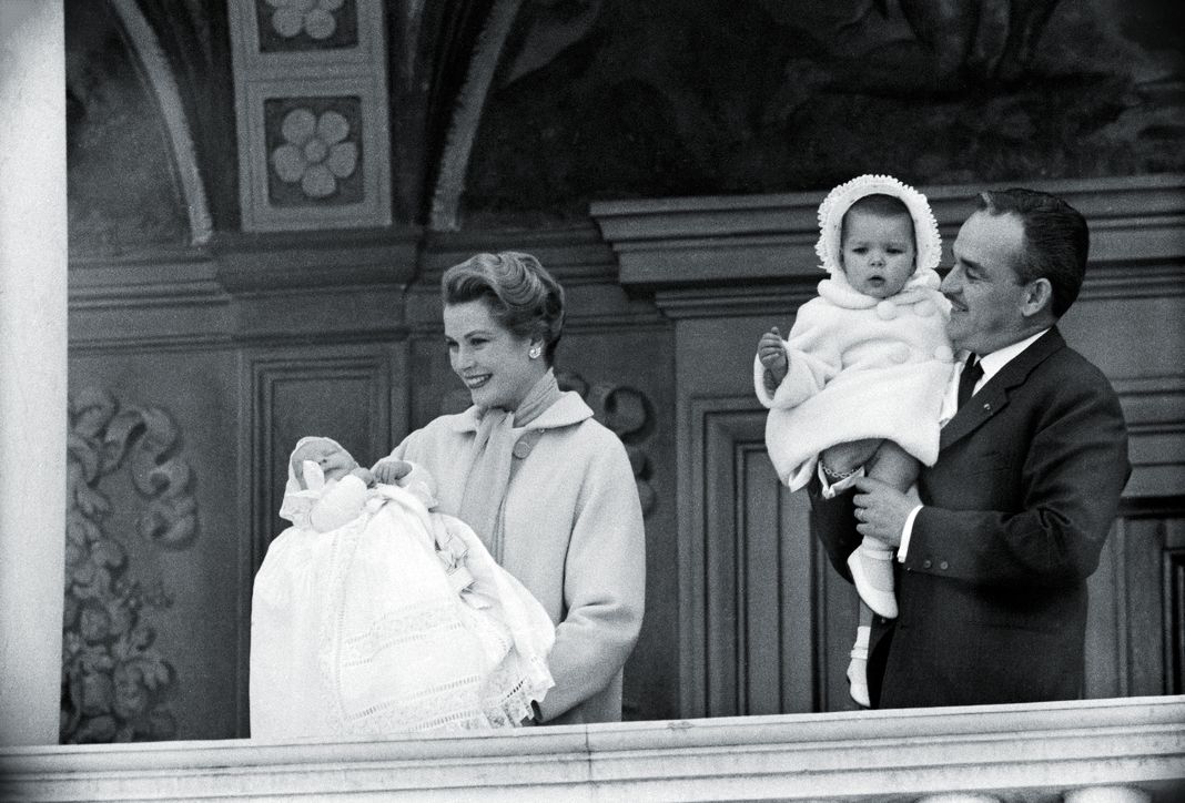 Ренье III, принц Монако, держит Каролину, принцессу Ганноверскую, а американская актриса Грейс Келли, принцесса Монако, представляет принца Альберта II с балкона Княжеского дворца.