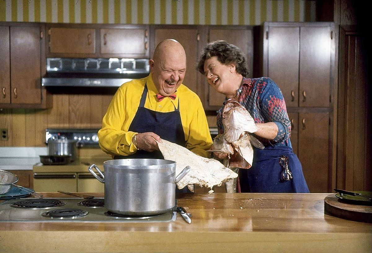 Джулия Чайлд и Джеймс Бирд вместе смеются, чистя большую рыбу, в телешоу «Революционные рецепты»