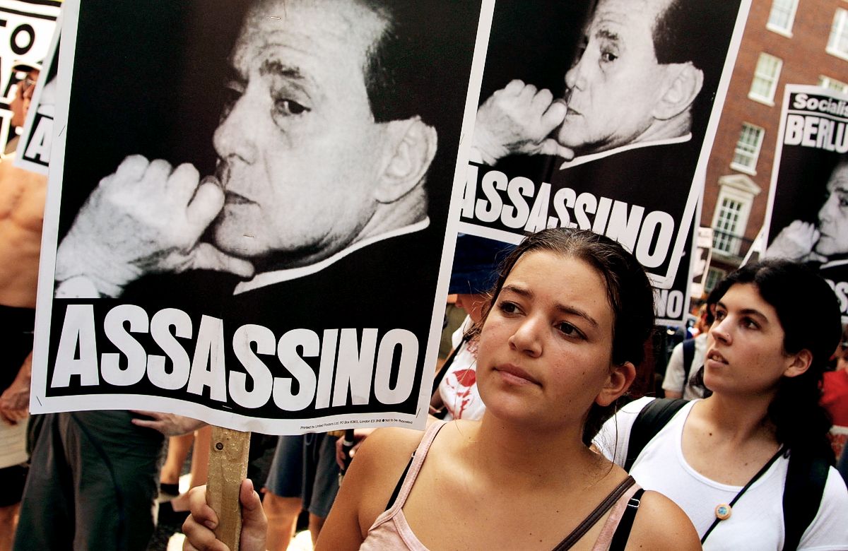 Протестующие несут плакаты, обвиняющие президента Италии Сильвио Берлускони в убийстве на демонстрации у посольства Италии